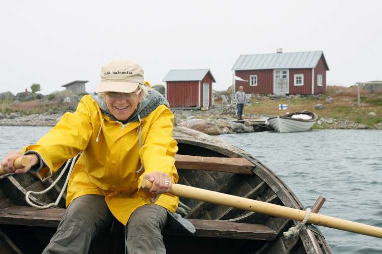 En kvinna i en gul regnjacka ror en båt vid Valsörarna.