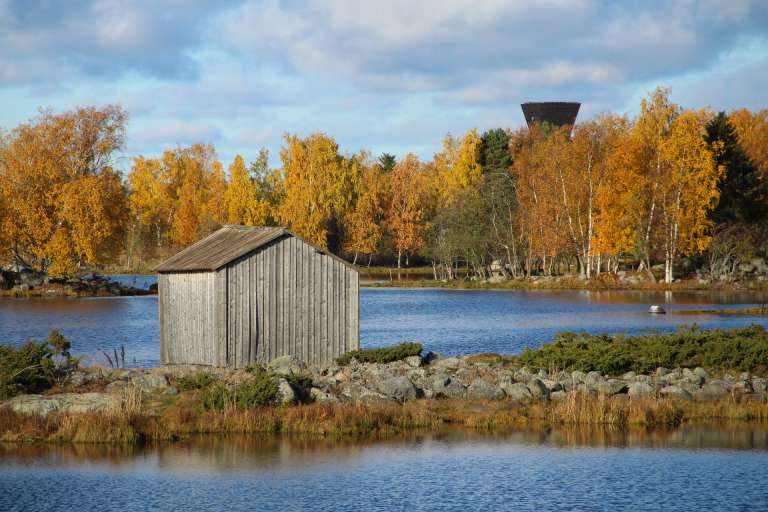 Utiktstornet Saltkaret och ett grå båthus i Bodbacks gamla hamnen i höstfärger.