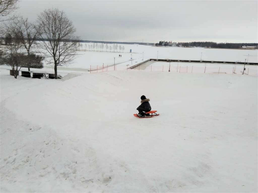 Lapsi laskee rattikelkalla pulkkamäkeä meren rannassa.