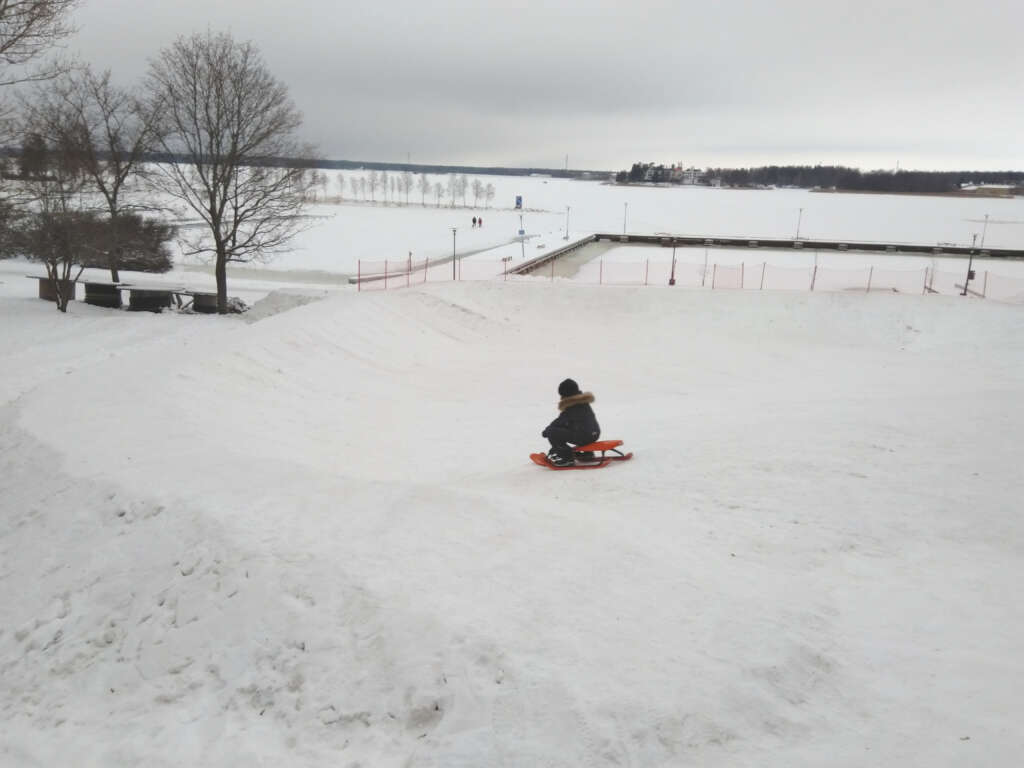 Lapsi laskee rattikelkalla mäkeä meren rannalla.