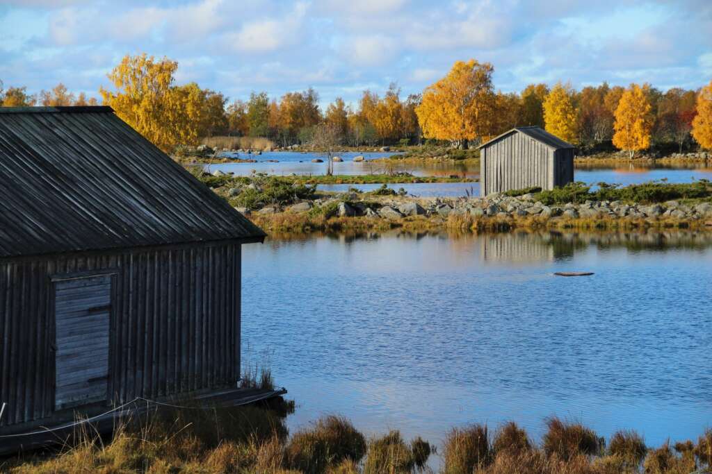 Kaksi harmaata venevajaa moreeniselänteiden päällä, veden ympäröimänä. Puissa on syysruska.