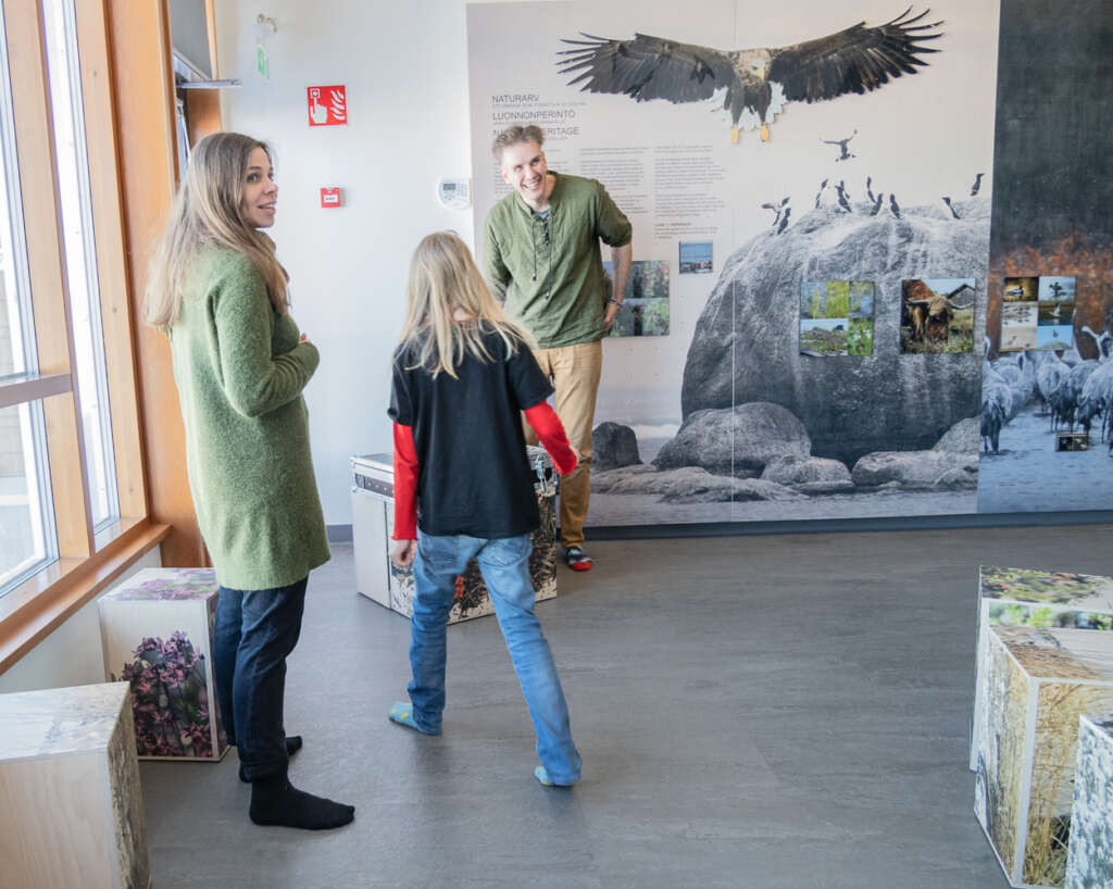 Two smiling adults look at the exhibition, and a child has back faced towards camera.