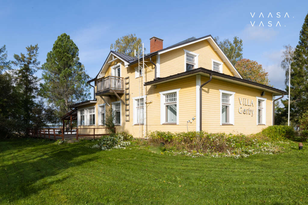 A yellow two-story villa with a large yard. The yard is lush and peaceful, with trees and a wide lawn.