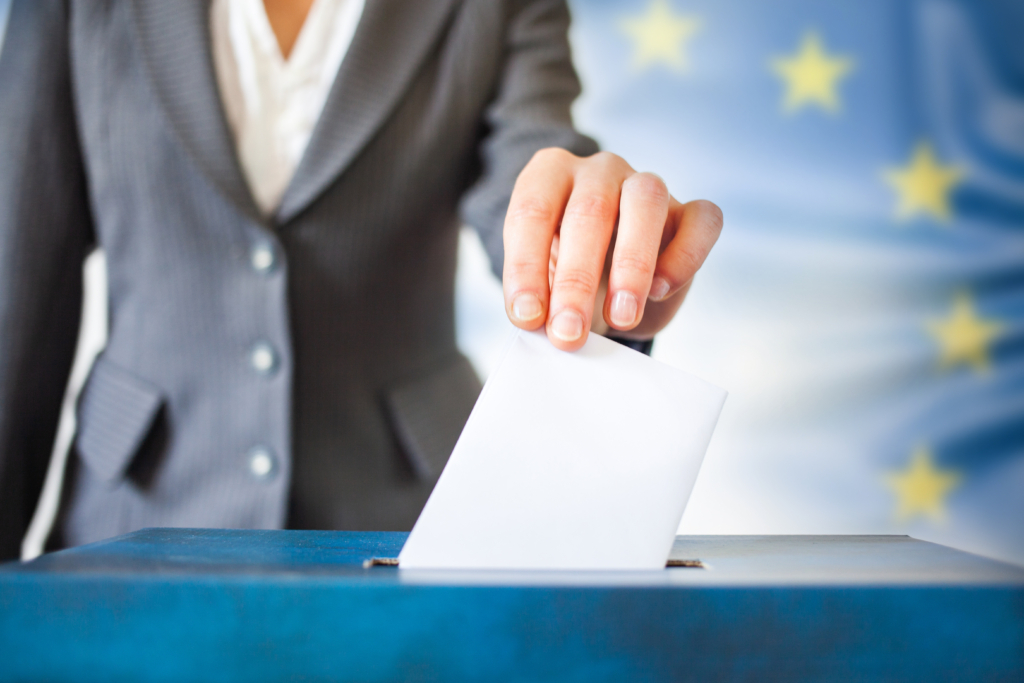 elections in European Union. The hand of woman putting her vote in the ballot box, EU flag in the background