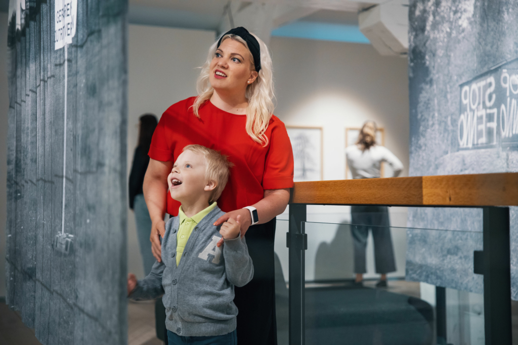 En mamma och ett barn tittar glatt på en målning i museet.