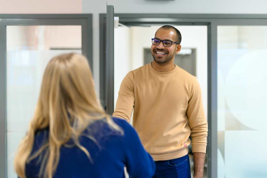 A smiling customer greets a customer service representative with a handshake at the office door.