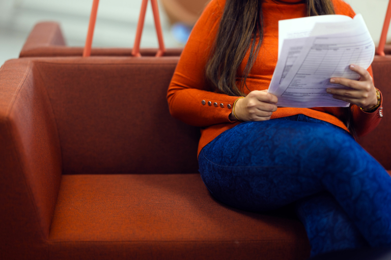 A person is sitting on a sofa holding papers in their hands.