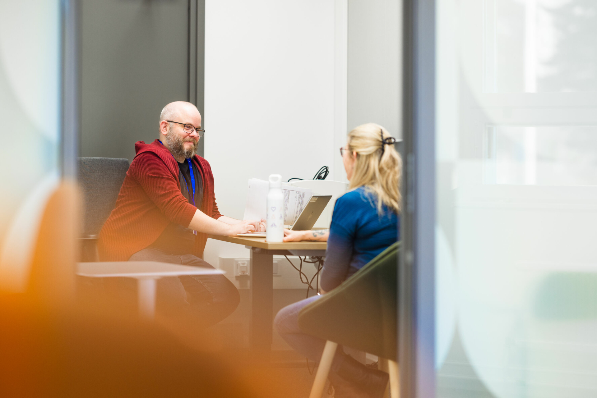 A customer service representative talks with a customer at a table in an office environment.