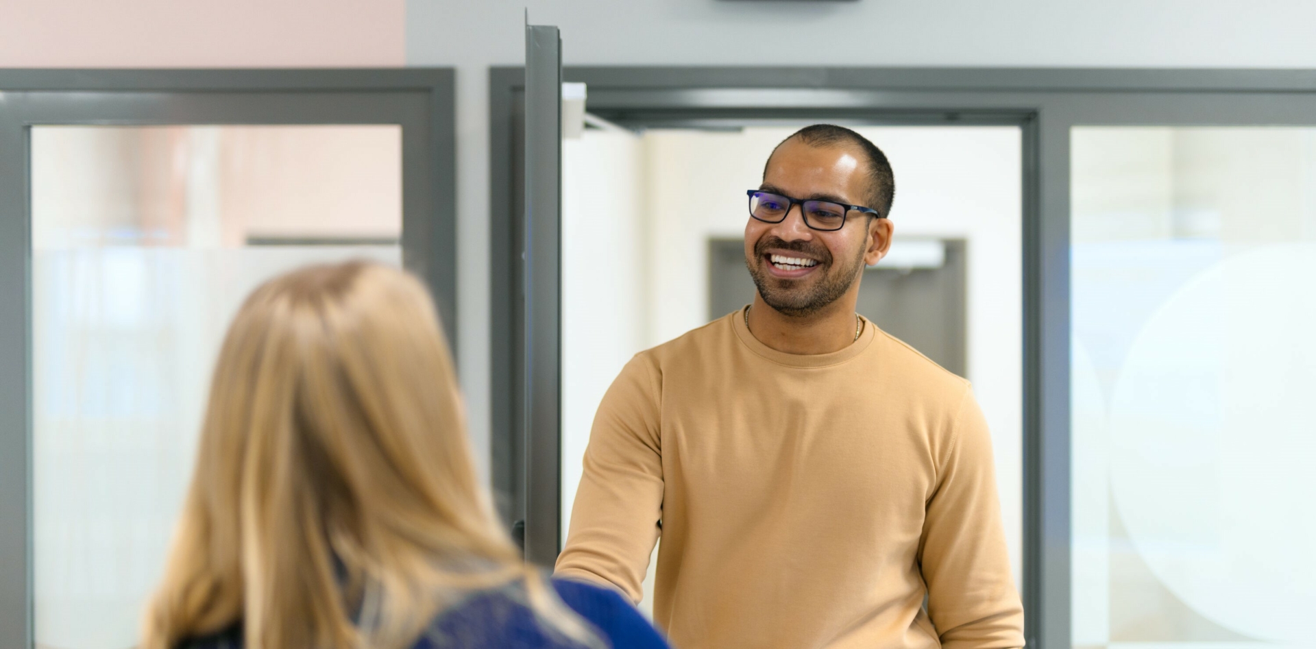 A smiling customer greets a customer service representative with a handshake at the office door.